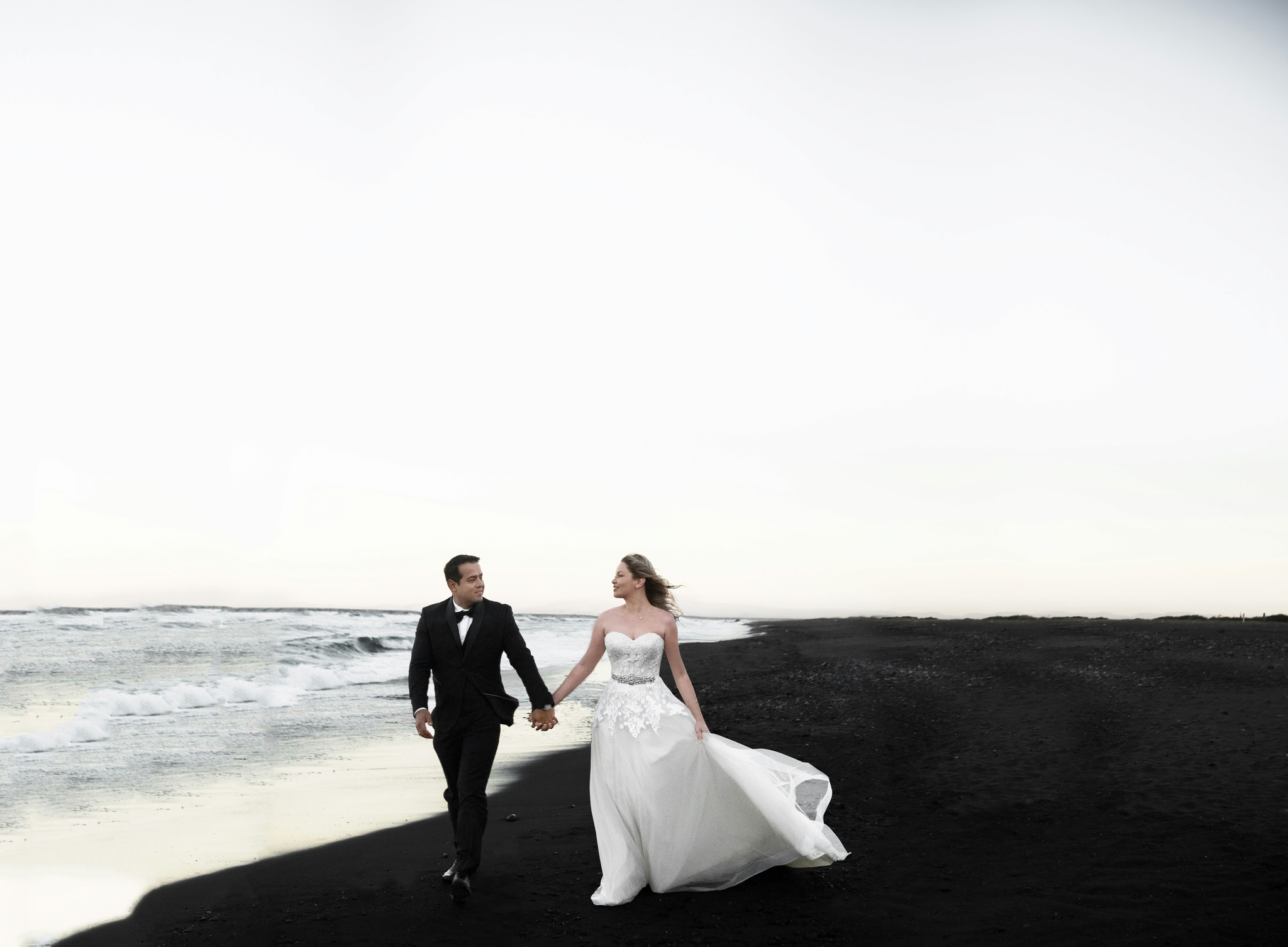 Wedding couple walking hand in hand along a black sand beach in South Iceland.